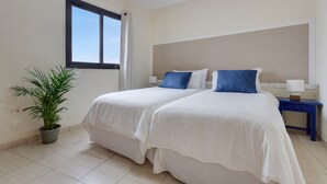 A hotel room with two beds, a potted plant, a window, and a nightstand with a lamp. - Luxury Penthouse Plaza Apartment with Mountain View, Private Terrace, and Wi-Fi (Playa San Juan)
