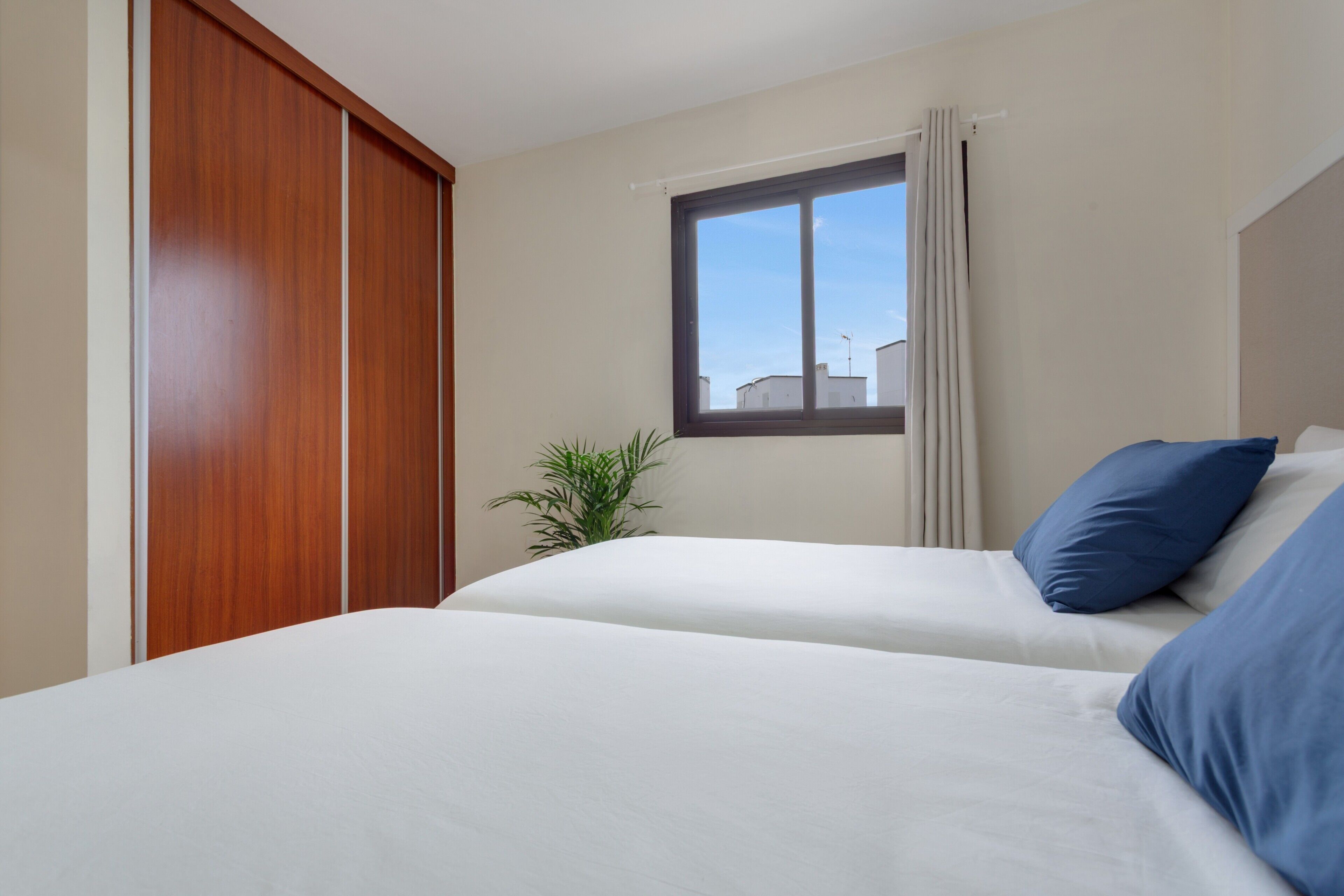 Una habitación de hotel con dos camas, un ventanal, una planta y un armario de madera.