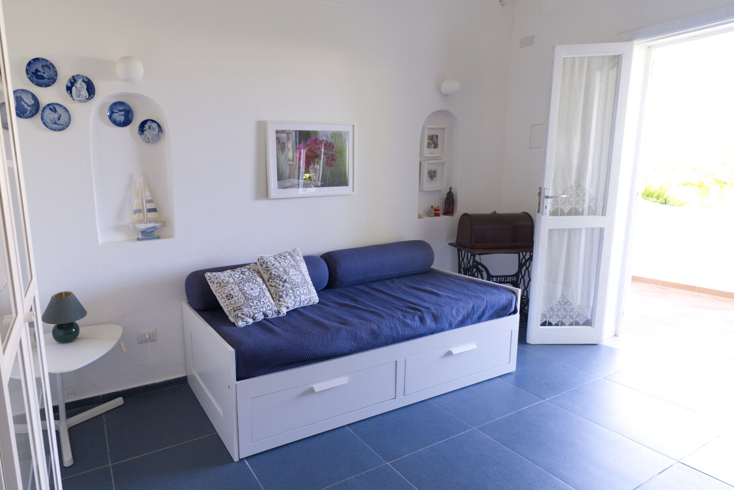 A bedroom with a bed, a small table, a sewing machine, and a window.