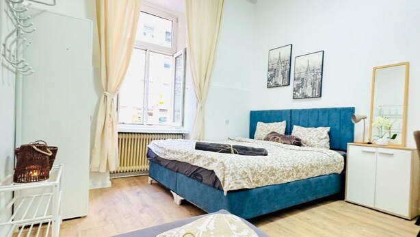 Une chambre à coucher avec un lit, une fenêtre avec des rideaux, un radiateur, une armoire blanche et un miroir.