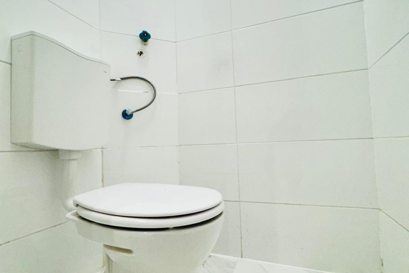 Eine weiße Toilette mit Tank, Wandspülknopf und sichtbarer Rohrleitung.