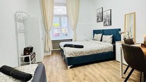 Une chambre à coucher comprenant un lit, un bureau, une chaise, un radiateur, une fenêtre avec des rideaux et un miroir fixé au mur.