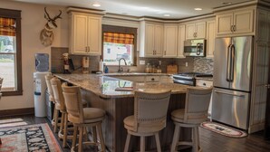 A modern kitchen with a central island, bar stools, stainless steel appliances, and a water dispenser.