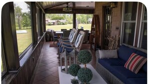 A covered porch with a dining area, seating, and potted plants.