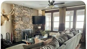 A living room with a stone fireplace, a large sofa, a mounted deer head, and a television.