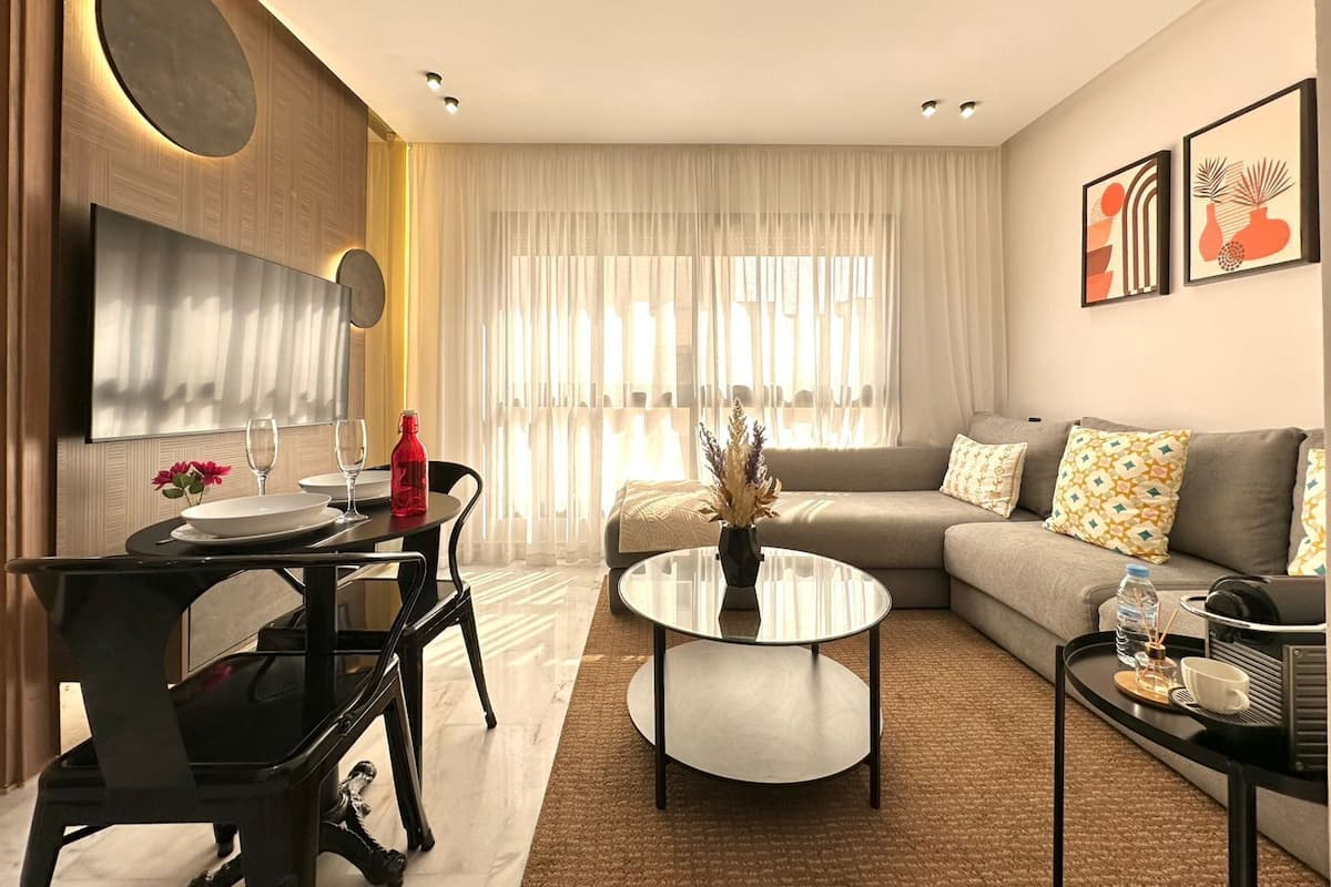 A modern living room with a sofa, a coffee table, a dining table with chairs, and a TV mounted on the wall.