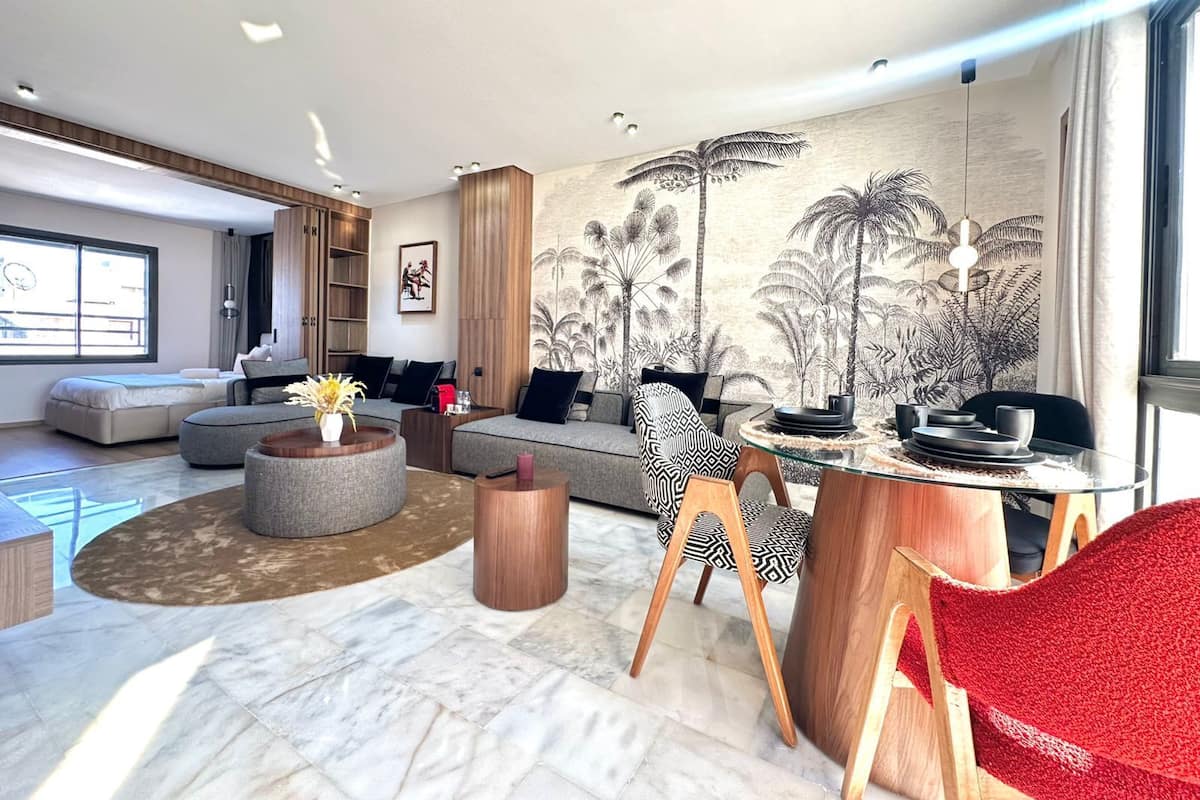A modern living room with a large sofa, a glass coffee table, and a dining area with a red chair.