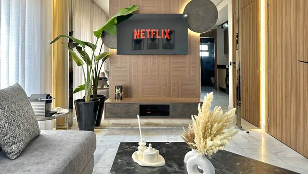 Una sala de estar moderna con un televisor de pantalla plana grande montado en una pared de madera, un sofá, una mesa de centro y plantas decorativas.