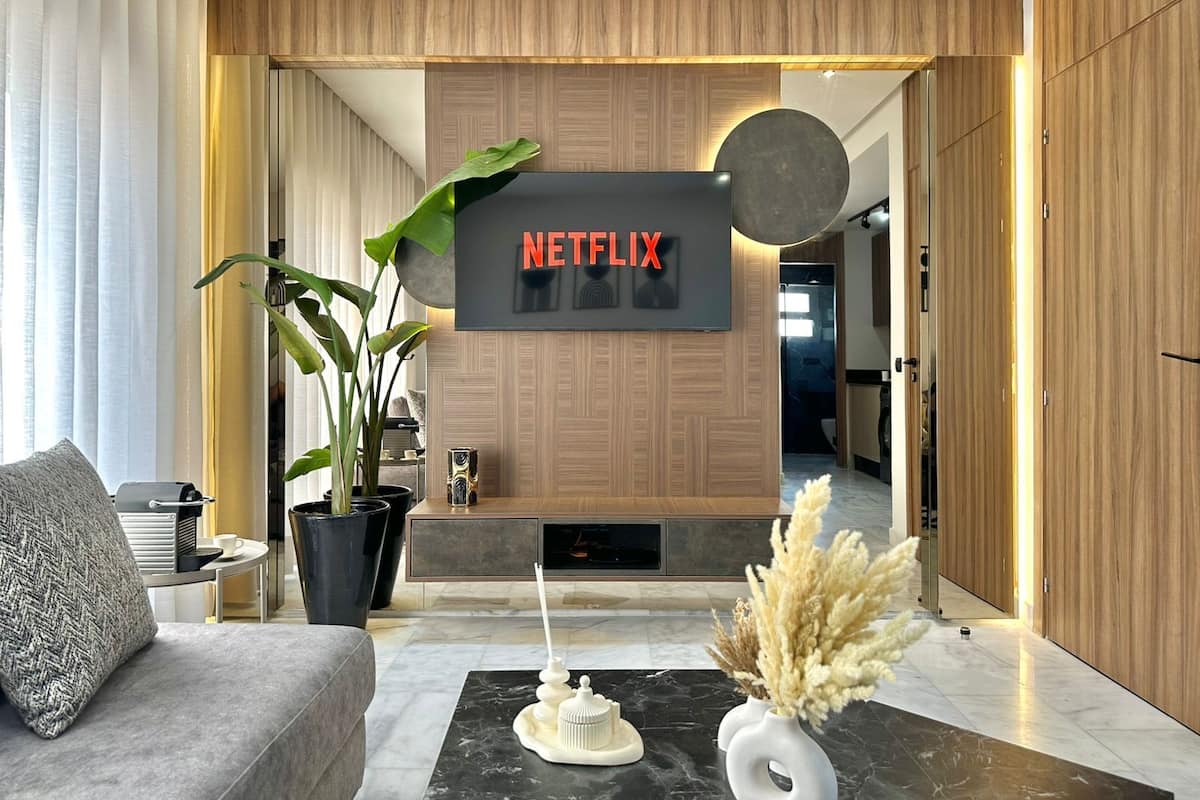 A modern living room with a large flat-screen TV mounted on a wooden wall, a sofa, a coffee table, and decorative plants.