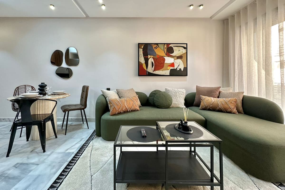 A modern living room with a green sofa, a glass coffee table, and a dining area with chairs and a table.