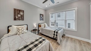 Ein Schlafzimmer mit zwei Betten, einem Deckenventilator und einem großen Fenster mit Jalousien.
