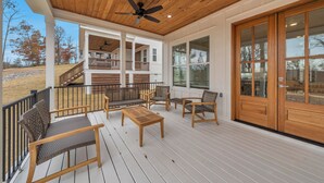 Eine überdachte Terrasse im Freien mit Holzmöbeln, einem Deckenventilator und großen Fenstern.