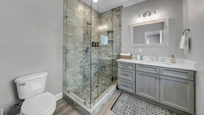 A bathroom with a glass-enclosed shower, a toilet, a vanity with a mirror, and a sink. - Cottages at Gunters Landing (Guntersville)