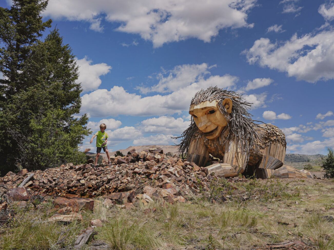 A large lion sculpture in a natural setting with a child nearby.