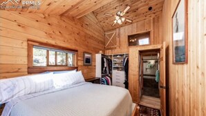 Un dormitorio tipo cabaña de madera con cama, armario y una ventana pequeña.