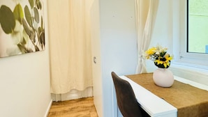 Une chambre avec un lit, une table de chevet ornée d’un vase de fleurs, une fenêtre avec des rideaux et une œuvre d’art accrochée au mur.