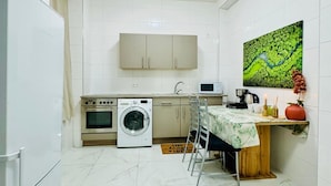 Une cuisine compacte équipée d’un lave-linge, d’un four à micro-ondes et d’un coin repas avec une table et des chaises.