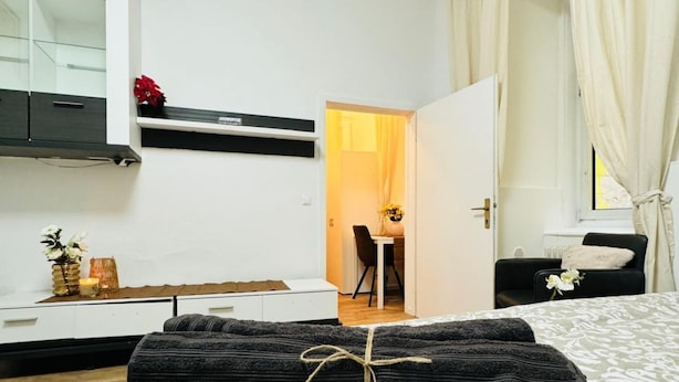 Une chambre d’hôtel avec un lit, un bureau, une chaise, une petite table avec un vase et une fenêtre avec des rideaux.