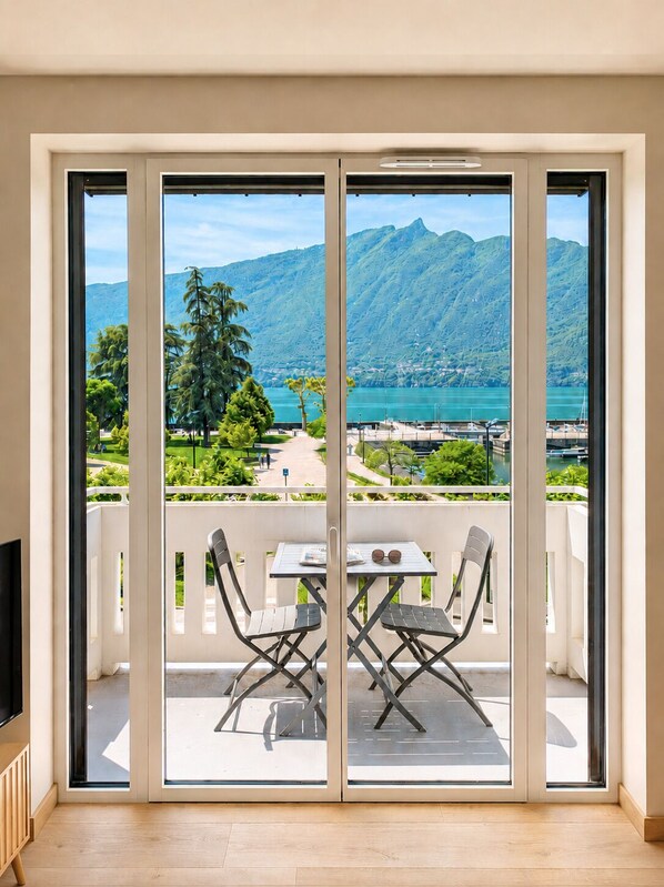 Un balcón con mesa y sillas, un televisor y vistas a un lago y montañas.