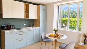 A modern kitchen with a dining area, a view of greenery, and a window. - L'Océan des Âges (T3 lake view) (Aix-les-Bains)