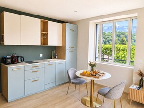 A modern kitchen with a dining area, a view of greenery, and a window. - L'Océan des Âges (T3 lake view) (Aix-les-Bains)