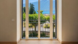 A room with a large sliding glass door leading to a balcony with a view of a mountain and lake. - L'Océan des Âges (T3 lake view) (Aix-les-Bains)