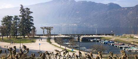A coastal area with a marina, a pedestrian path, and mountains in the background.