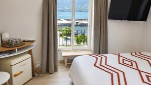 Ein Hotelzimmer mit Bett, Schreibtisch mit Tablett und Fernseher, sowie einem Fenster mit Vorhängen.