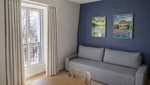 A modern living room with a grey sofa, a round wooden table, and two framed posters on the wall. - L'Ecume des Ondes (T2 mountain view) (Aix-les-Bains)