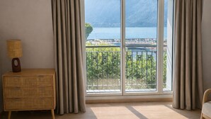 A room with a large sliding glass door leading to a balcony with a view of a lake and mountains. - Les Flots Harmonieux (30m² lake view) (Aix-les-Bains)