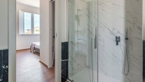Un bagno moderno con cabina doccia in vetro, pareti in marmo e pavimento in legno.