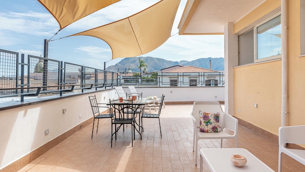 Una terrazza sul tetto con tavolo e sedie, un'ampia tenda da sole e vista su edifici e montagne sullo sfondo.