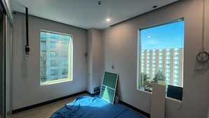 A modern bedroom with large windows, a bed, and a view of a building. - Rook Hotel   (Mississauga)
