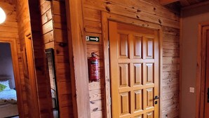Interior de madera con un extintor montado en la pared, una puerta con ventana y señal de salida visible.