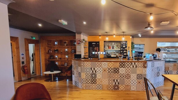 Un restaurante acogedor con una zona de bar, estanterías de madera y un revestimiento de azulejos estampados.