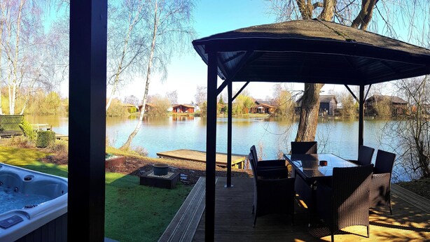 Un jacuzzi y zona de estar al aire libre con vista a un lago y casas al fondo.