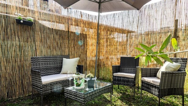 An outdoor patio with wicker furniture, a glass table, and a bamboo fence. - Volta hub- parking lot and garden Lake Como 7min (Como)