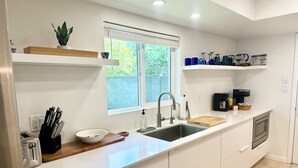 A modern kitchen with white cabinets, a stainless steel sink, a coffee maker, and a window with blinds. - Family-friendly 4 bd with sparkling free heated pool, , games. ASU close (Tempe)