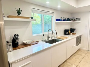 A modern kitchen with white cabinets, a stainless steel sink, a coffee maker, and a window with blinds.