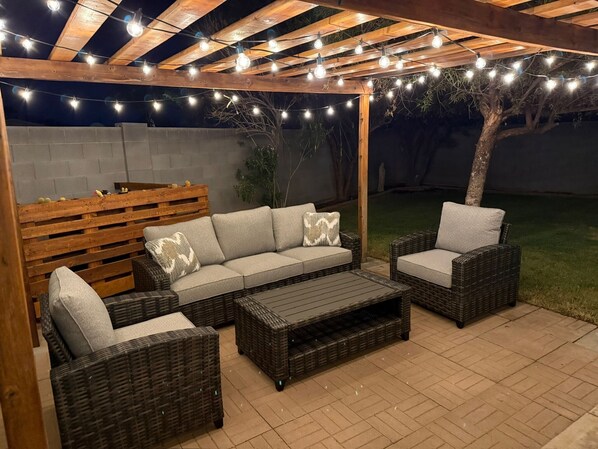 An outdoor patio with wicker furniture, string lights, and a wooden pergola.