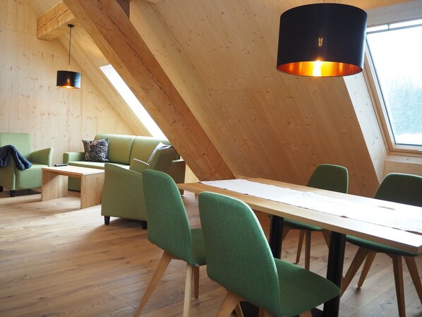 A modern interior with a sloped ceiling, wooden beams, a dining table with chairs, and a sofa.