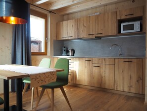 A compact kitchen with wooden cabinets, a built-in microwave, a stainless steel sink, and a dining area with a table and chairs.