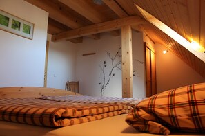A bedroom with a wooden ceiling, a bed with plaid bedding, a wall-mounted branch decoration, and a door.