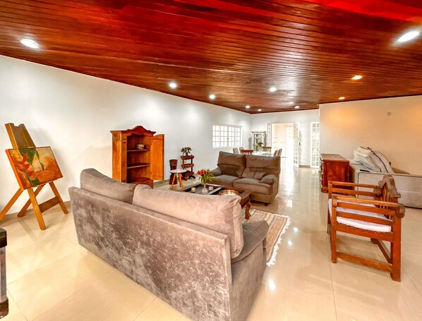 A spacious living room with a wooden ceiling, a grey sofa, a wooden cabinet, and a painting on easels. - Casa Alto Padr o com Piscina no Alto da Lapa (São Paulo)