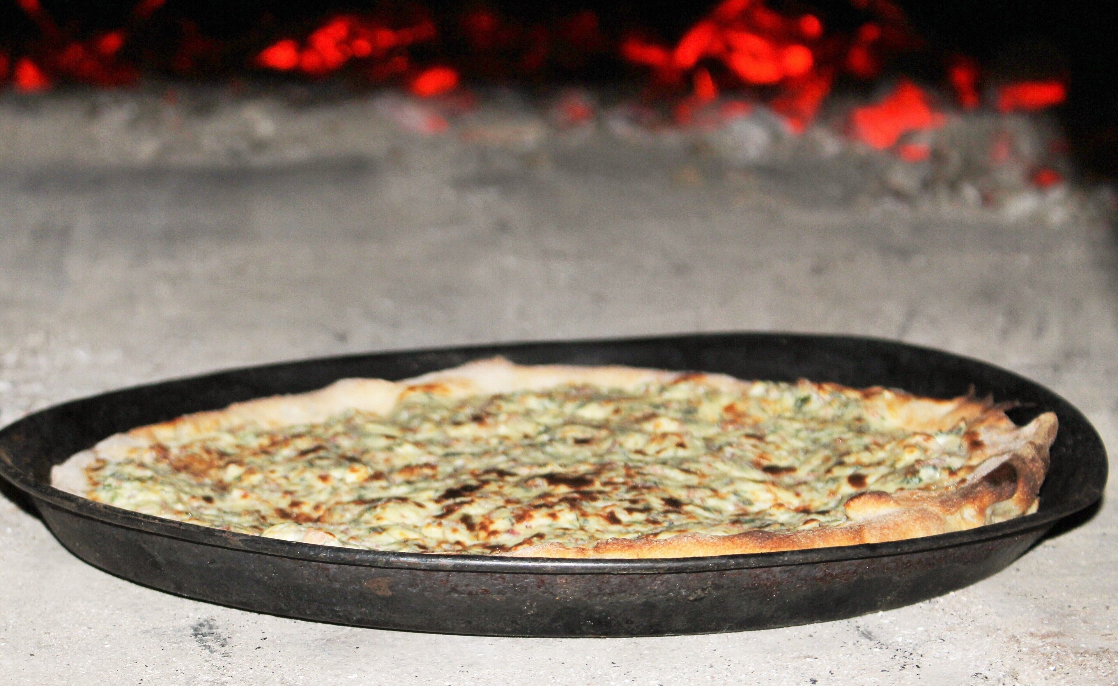 Eine Pizza in einer schwarzen Pfanne auf einer Arbeitsplatte.