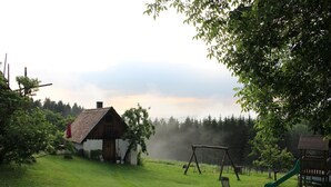 A rustic wooden house with a sloped roof, a swing set, and a slide in a grassy yard.
