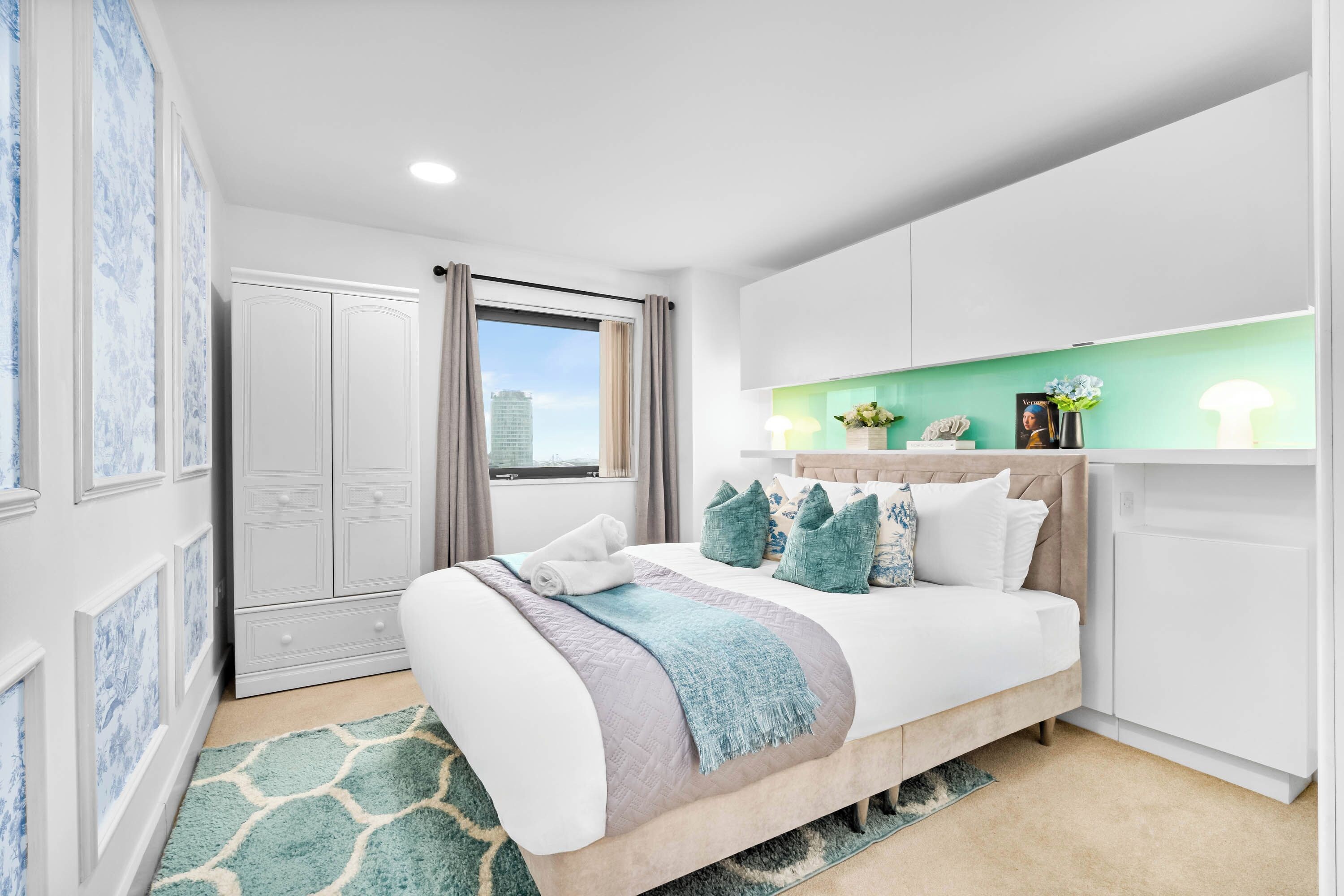 Une chambre à coucher moderne, avec un lit, une table de chevet, une fenêtre avec des rideaux et une vue sur un bâtiment à l’extérieur.