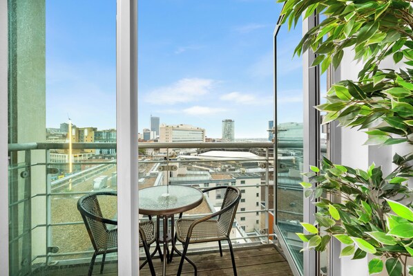 A balcony with a glass railing, two wicker chairs, a small round table, and a potted plant.
