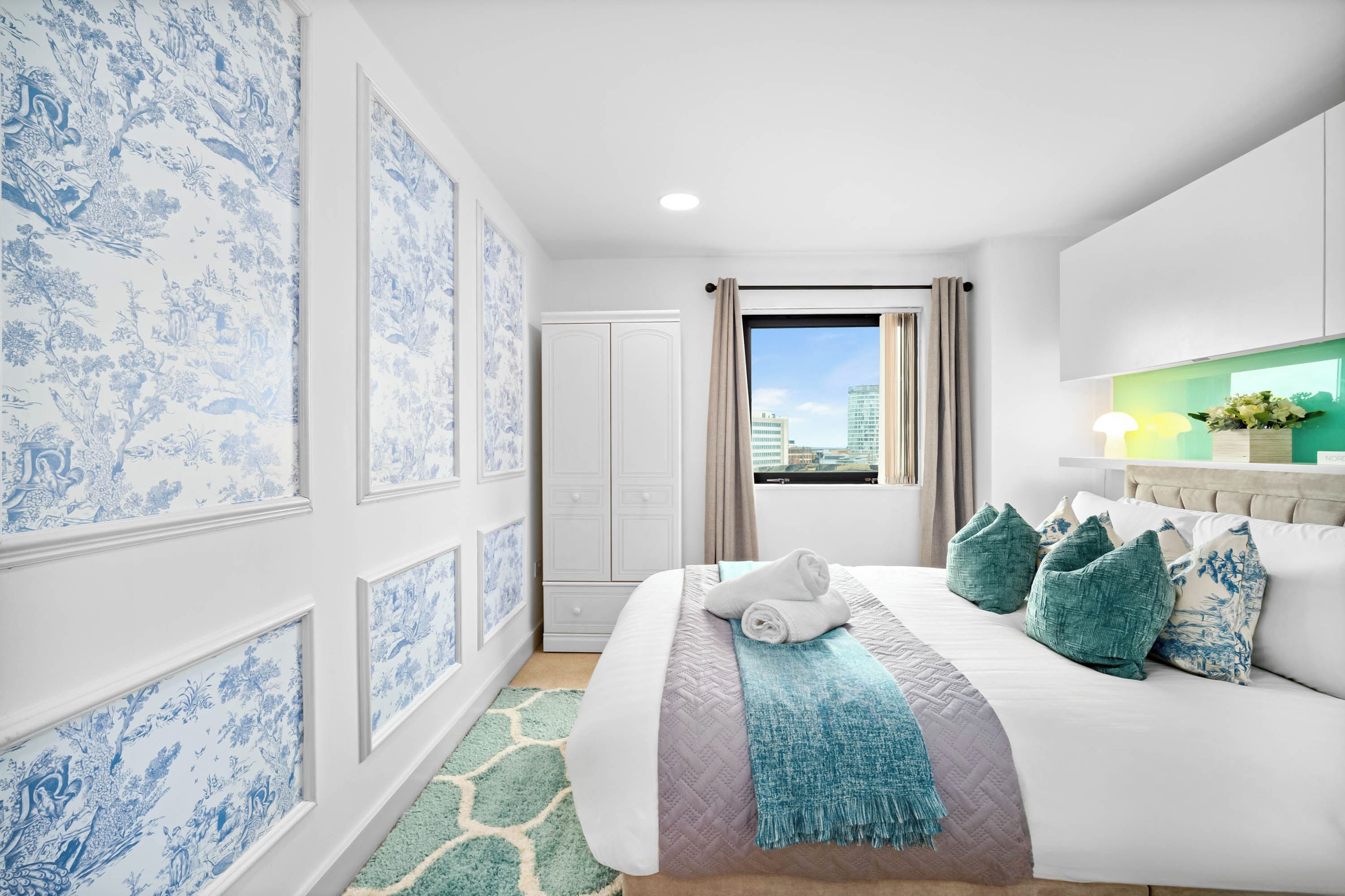 A hotel room with a large bed, a view of the city, and a bathroom with a white door.