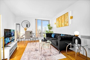 A modern living room with a black sofa, a glass coffee table, and a TV on a stand.